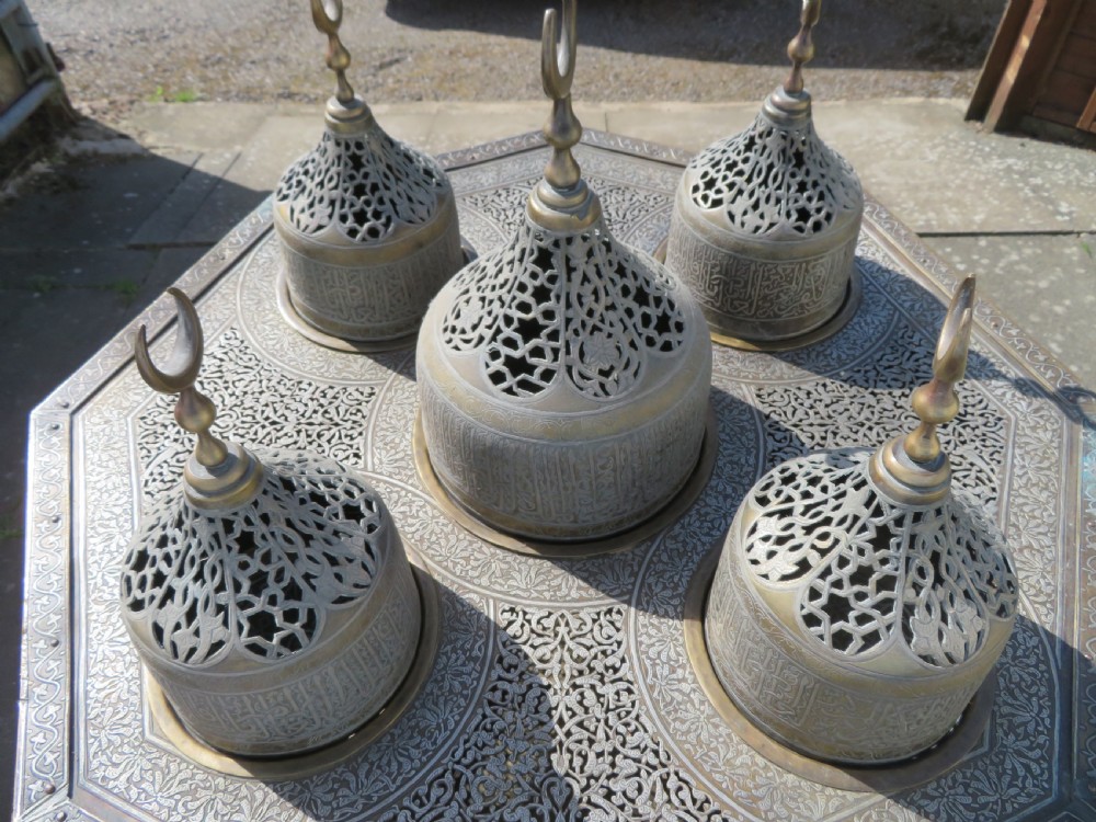 An octagonal brass and copper Cairoware Quran stand featuring Arabic calligraphy, pierced fretwork panels, silver inlay, and top dome finials crowned with crescent moons. View XIV