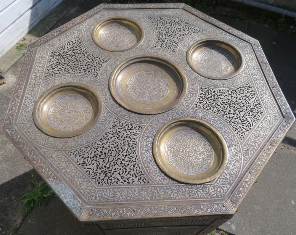 An octagonal brass and copper Cairoware Quran stand featuring Arabic calligraphy, pierced fretwork panels, silver inlay, and top dome finials crowned with crescent moons. View XVII