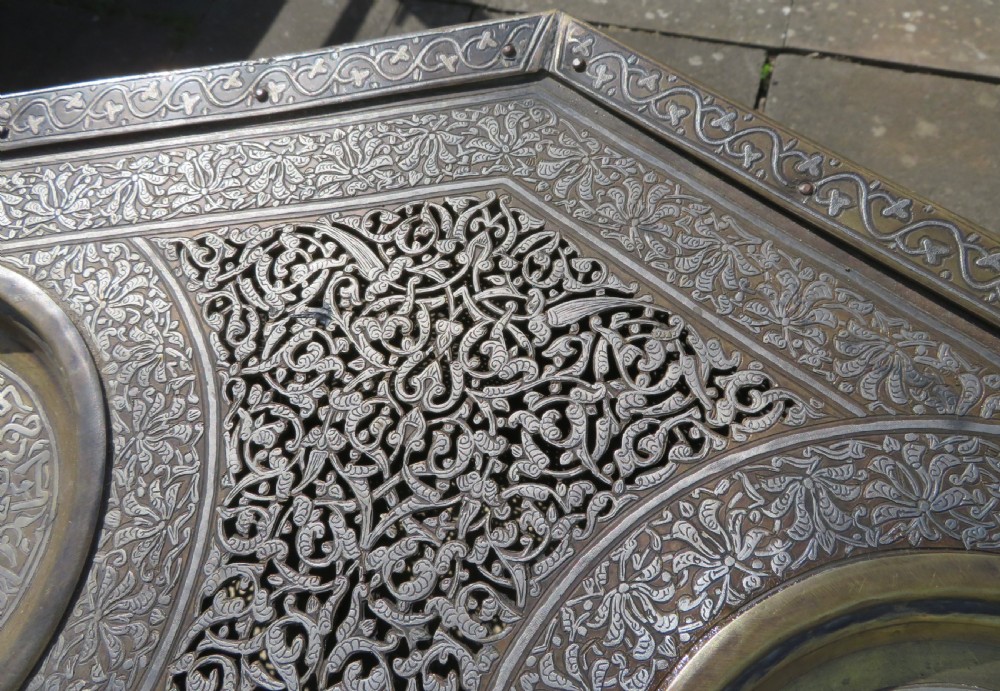 An octagonal brass and copper Cairoware Quran stand featuring Arabic calligraphy, pierced fretwork panels, silver inlay, and top dome finials crowned with crescent moons. View XIX