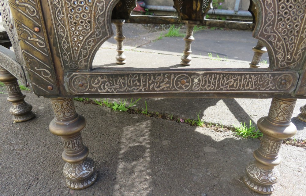 An octagonal brass and copper Cairoware Quran stand featuring Arabic calligraphy, pierced fretwork panels, silver inlay, and top dome finials crowned with crescent moons. View XX