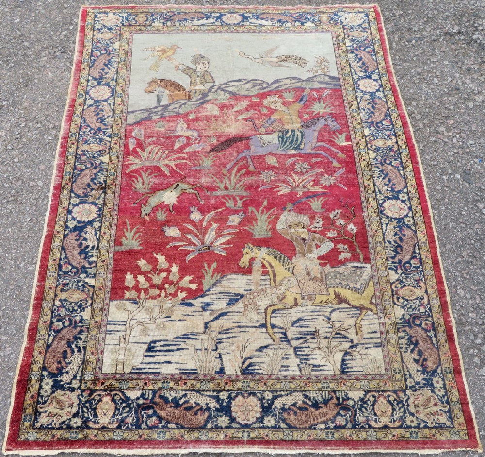 A 19th-century West Anatolian silk rug featuring a red central panel depicting horseback hunters, surrounded by a floral and animal motif navy border.