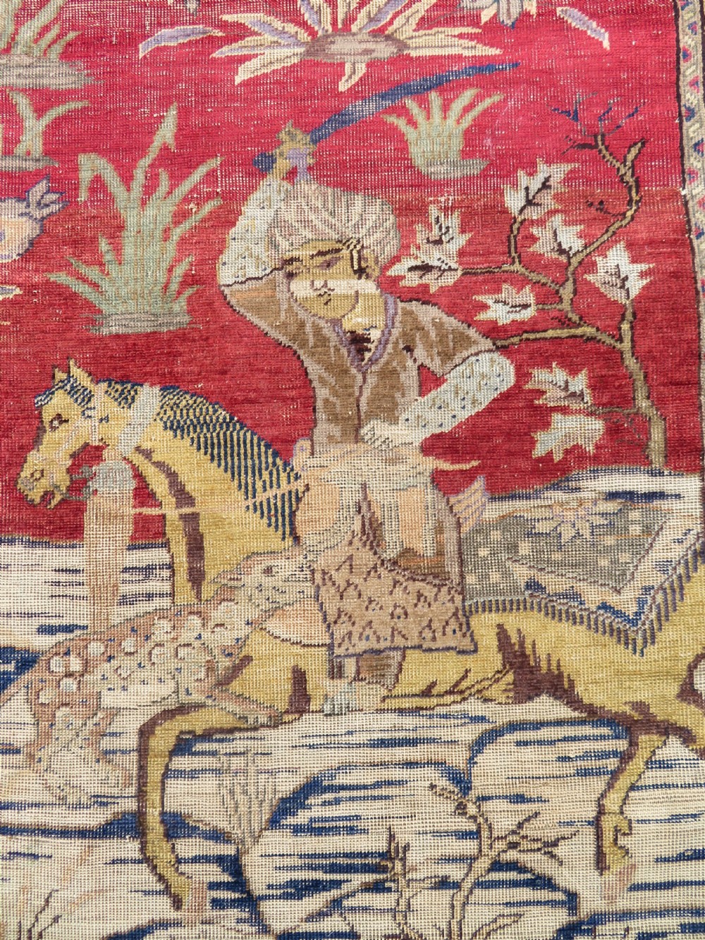 A 19th-century West Anatolian silk rug featuring a red central panel depicting horseback hunters, surrounded by a floral and animal motif navy border. View III