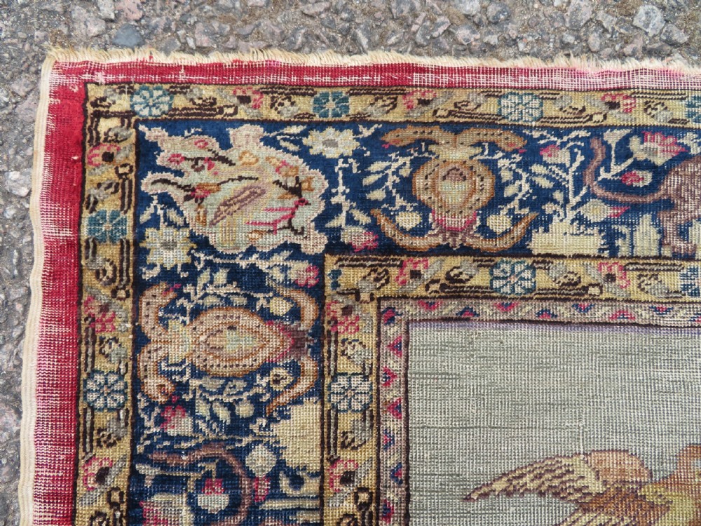 A 19th-century West Anatolian silk rug featuring a red central panel depicting horseback hunters, surrounded by a floral and animal motif navy border. View VI