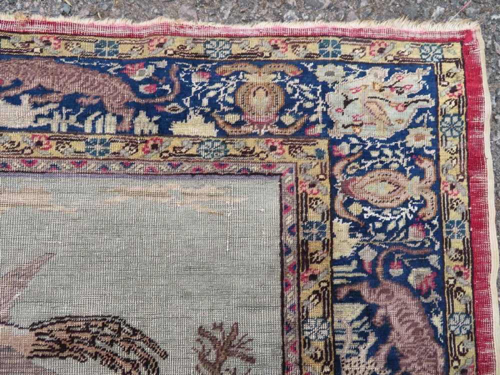 A 19th-century West Anatolian silk rug featuring a red central panel depicting horseback hunters, surrounded by a floral and animal motif navy border. View VII