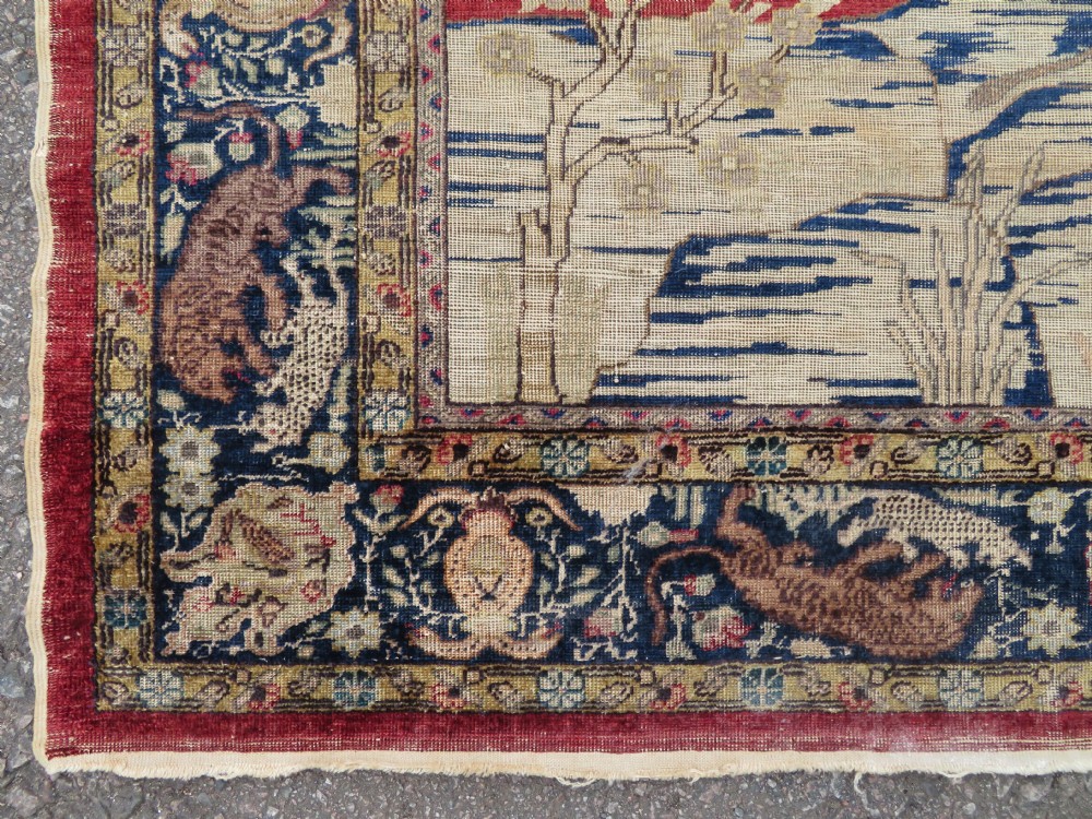A 19th-century West Anatolian silk rug featuring a red central panel depicting horseback hunters, surrounded by a floral and animal motif navy border. View XI