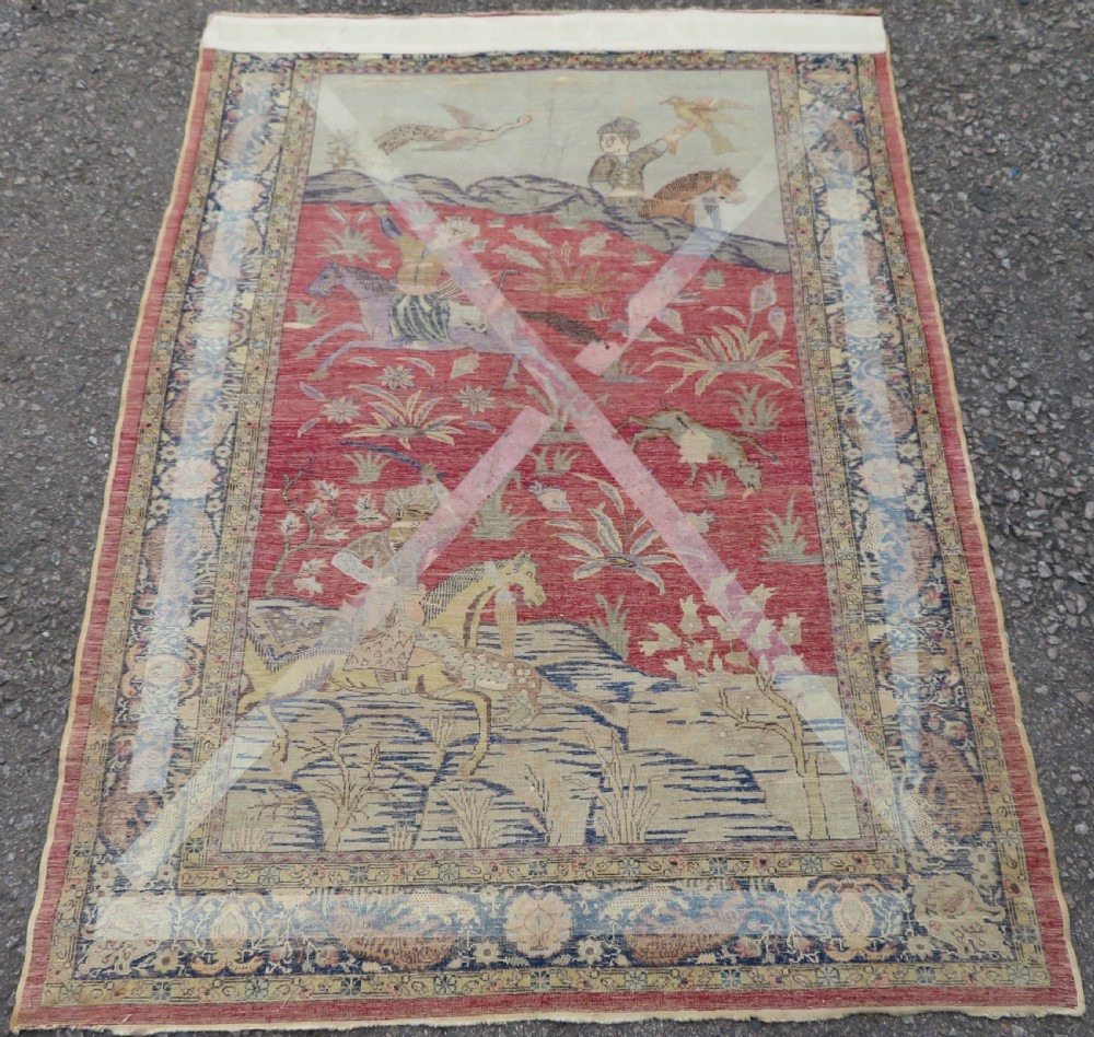 A 19th-century West Anatolian silk rug featuring a red central panel depicting horseback hunters, surrounded by a floral and animal motif navy border. View XII