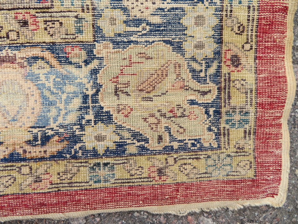 A 19th-century West Anatolian silk rug featuring a red central panel depicting horseback hunters, surrounded by a floral and animal motif navy border. View XIII