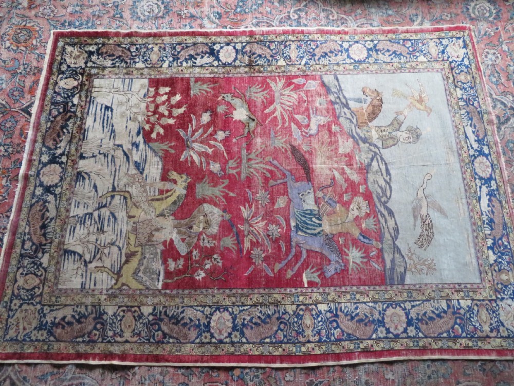 A 19th-century West Anatolian silk rug featuring a red central panel depicting horseback hunters, surrounded by a floral and animal motif navy border. View XVII