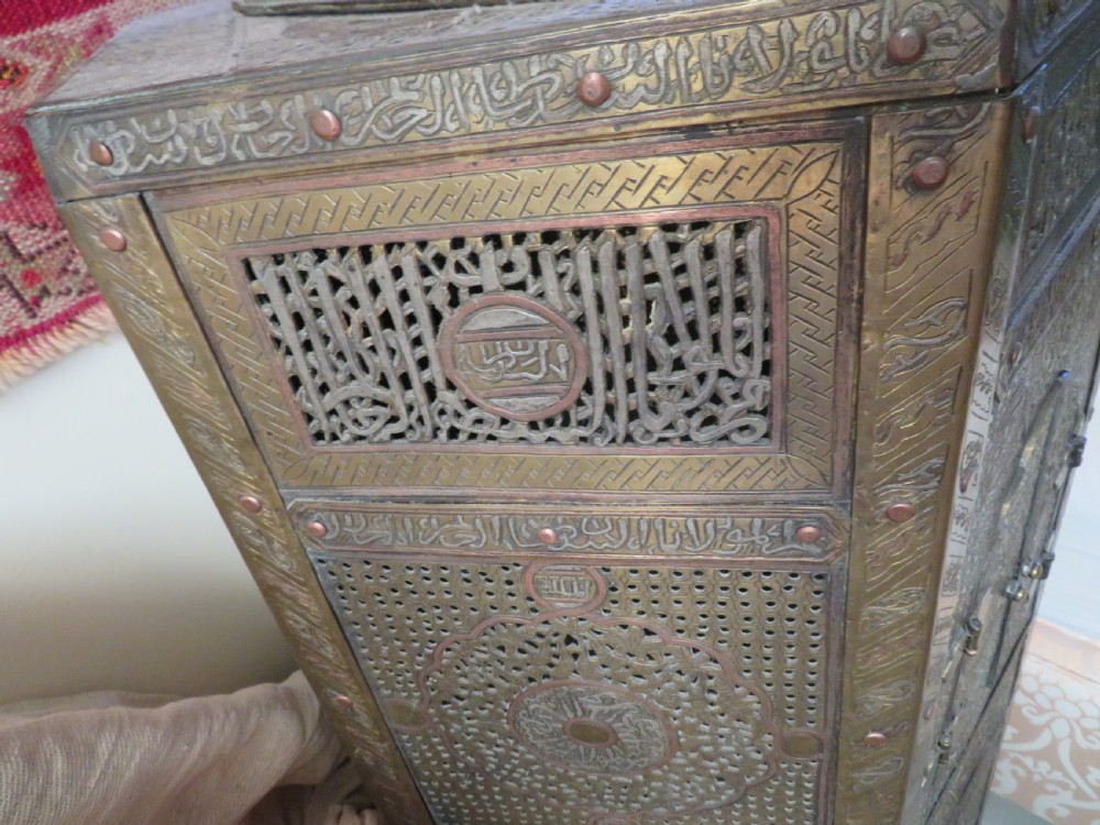 A hexagonal antique brass occasional table with pierced openwork panels, Arabic calligraphic inlays in copper and white metal, and double cabinet doors. View X