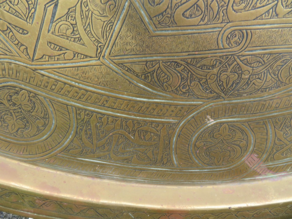 A large circular brass tray featuring detailed hand-engraved Islamic calligraphy, geometric interlace patterns, and a central star motif. View VIII