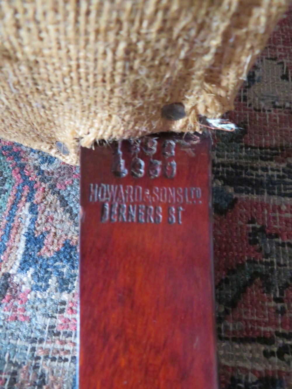 An antique Howard and Sons wingback armchair frame with exposed original stuffing, hessian backing, and square tapered wooden legs with castors. View IX