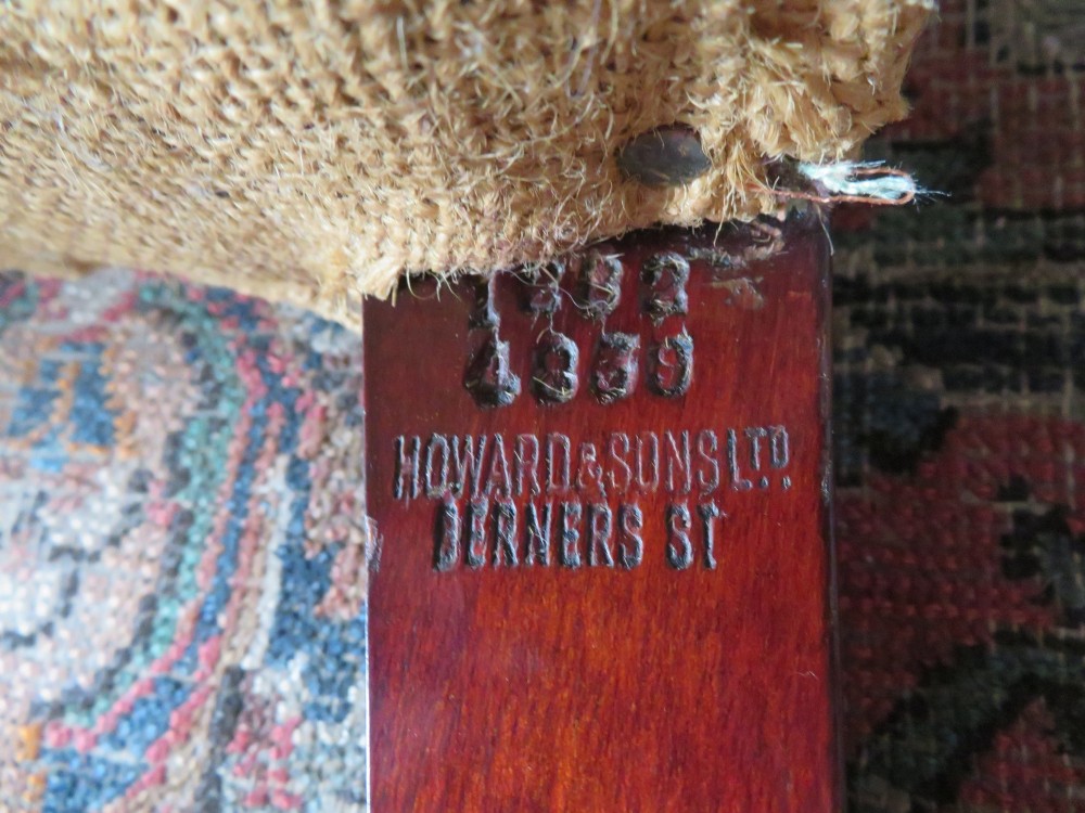An antique Howard and Sons wingback armchair frame with exposed original stuffing, hessian backing, and square tapered wooden legs with castors. View X