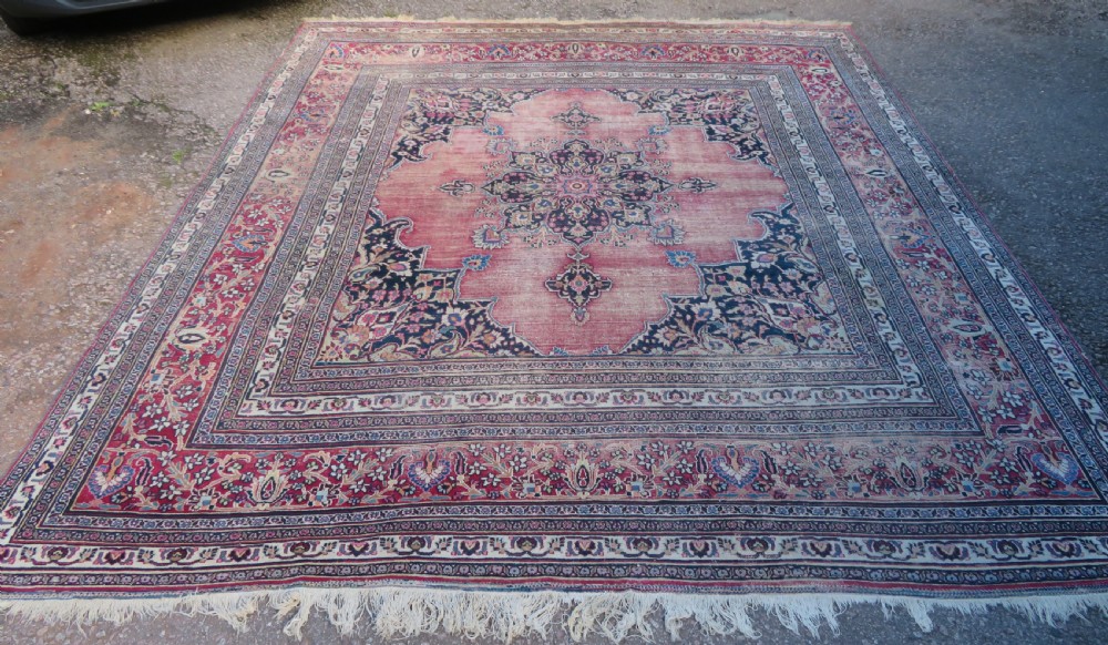An antique hand-knotted Meshed Persian wool carpet featuring a central navy blue medallion on a distressed rose pink field surrounded by intricate floral borders.