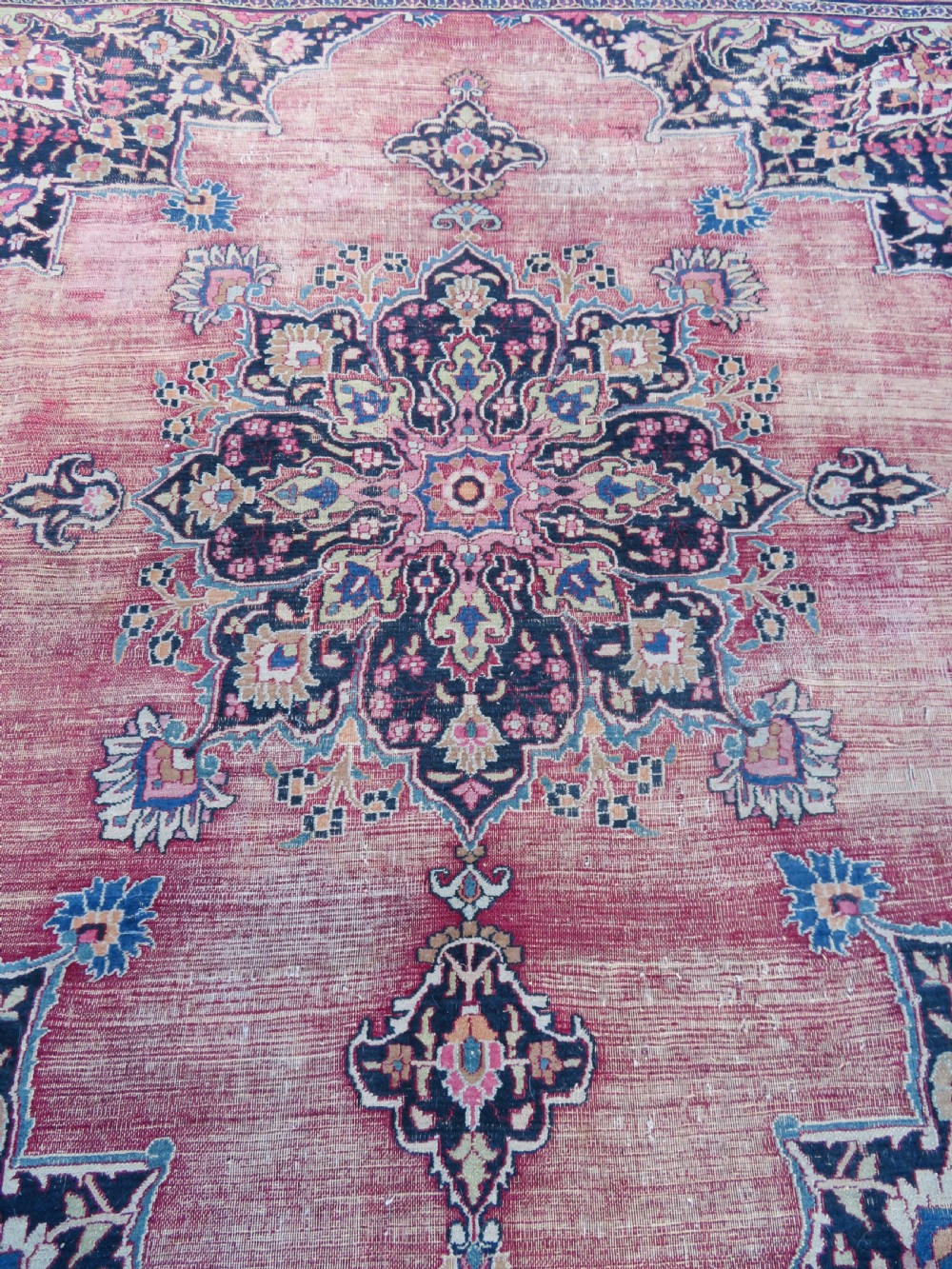 An antique hand-knotted Meshed Persian wool carpet featuring a central navy blue medallion on a distressed rose pink field surrounded by intricate floral borders. View V