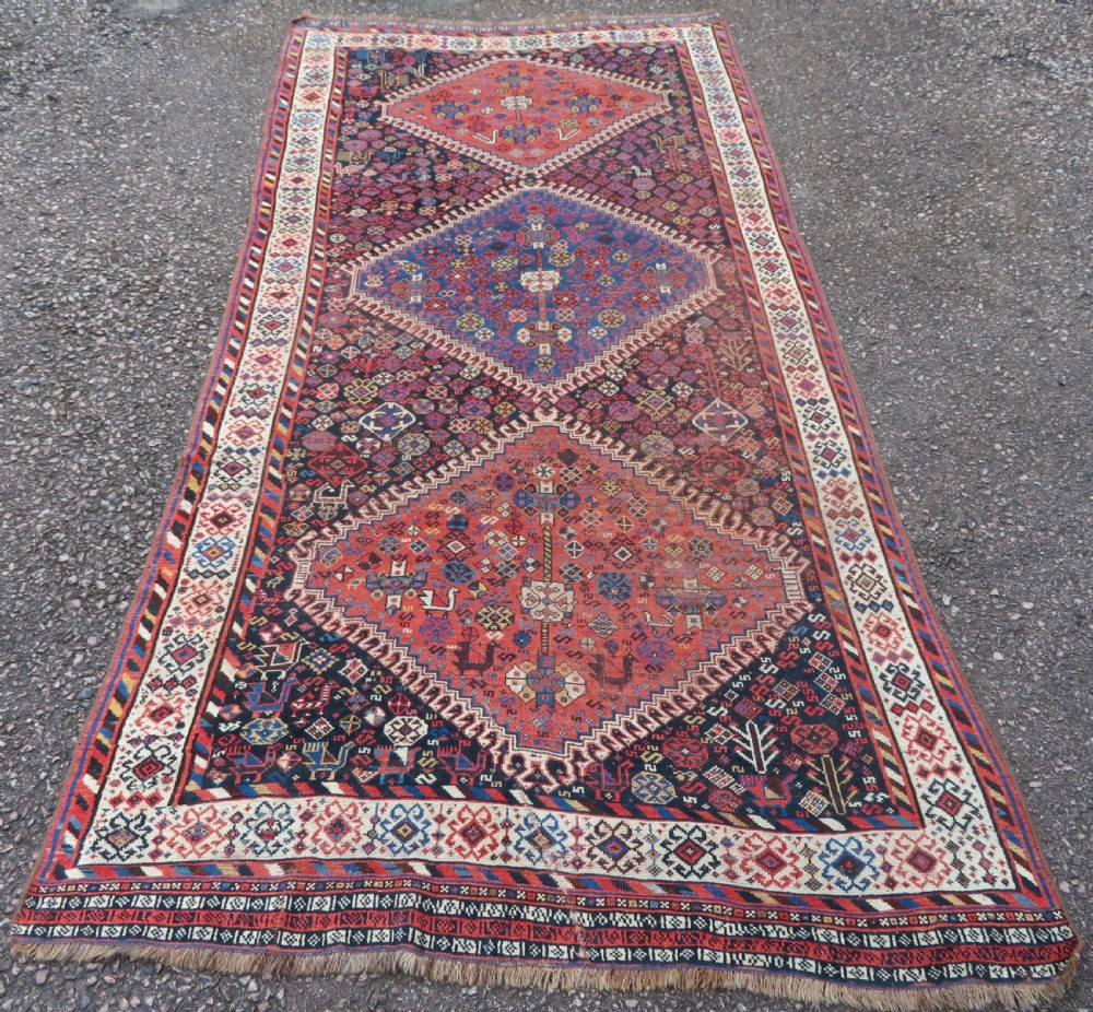 An antique Persian Luri hand-knotted wool carpet featuring three central diamond medallions surrounded by geometric tribal motifs and multi-banded borders.