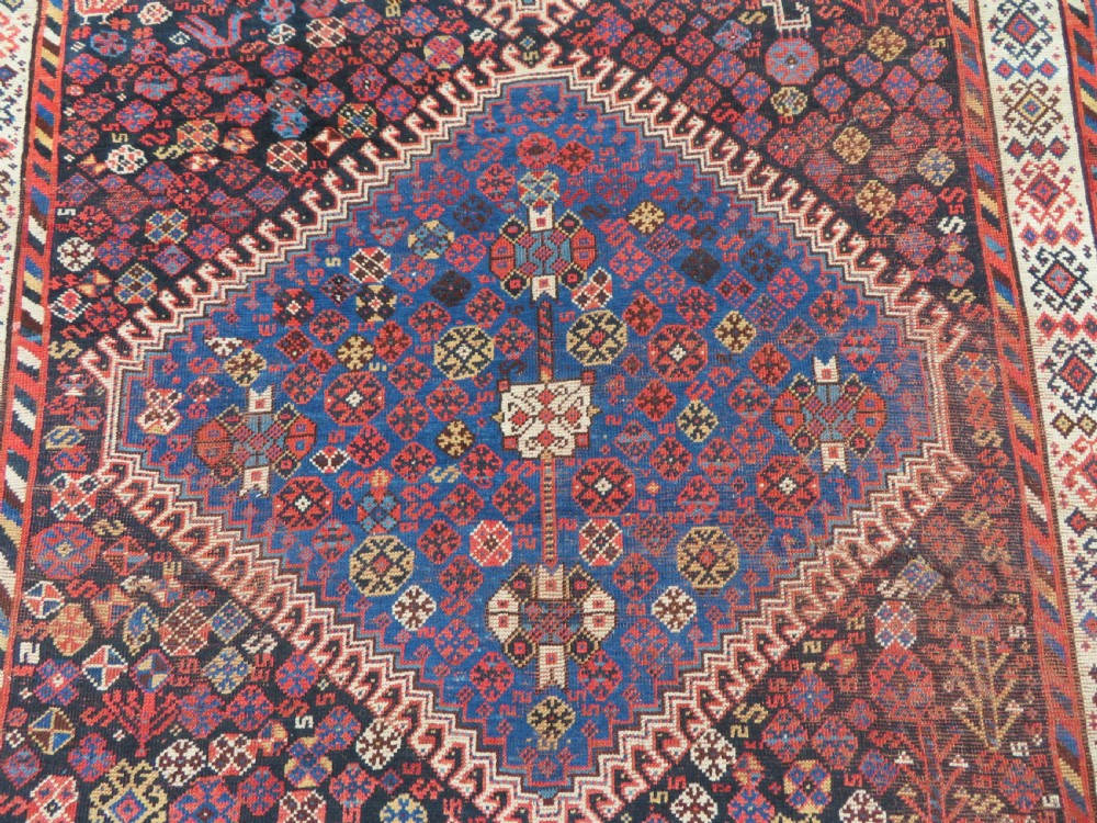 An antique Persian Luri hand-knotted wool carpet featuring three central diamond medallions surrounded by geometric tribal motifs and multi-banded borders. View IV
