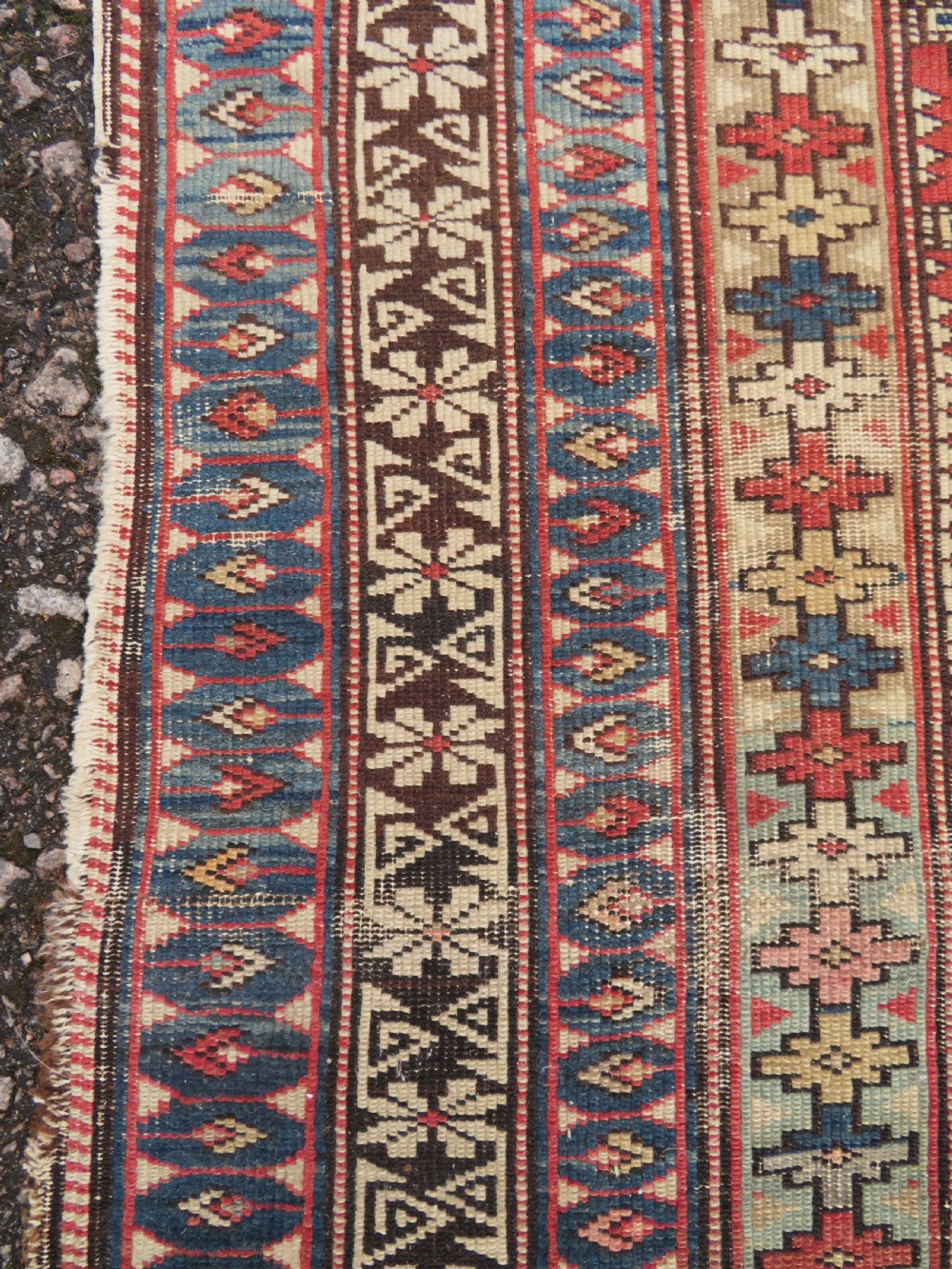 A distressed antique hand-knotted Caucasian Daghestan wool rug featuring geometric medallions and intricate borders in terracotta red, cream, and indigo blue. View IV