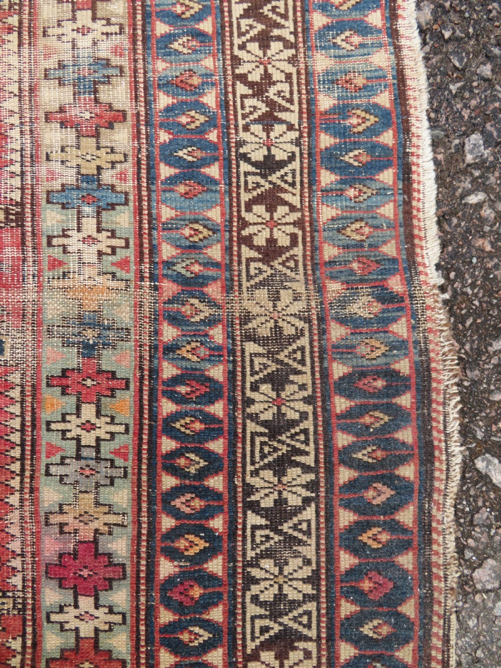 A distressed antique hand-knotted Caucasian Daghestan wool rug featuring geometric medallions and intricate borders in terracotta red, cream, and indigo blue. View VII