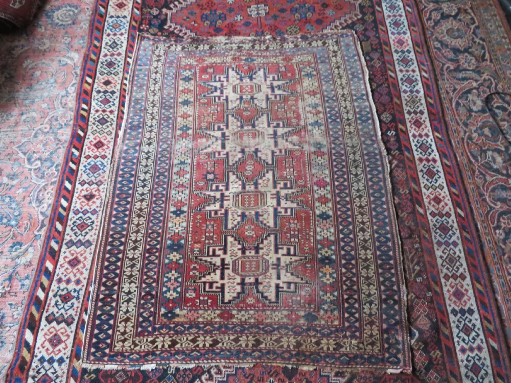 A distressed antique hand-knotted Caucasian Daghestan wool rug featuring geometric medallions and intricate borders in terracotta red, cream, and indigo blue. View XII