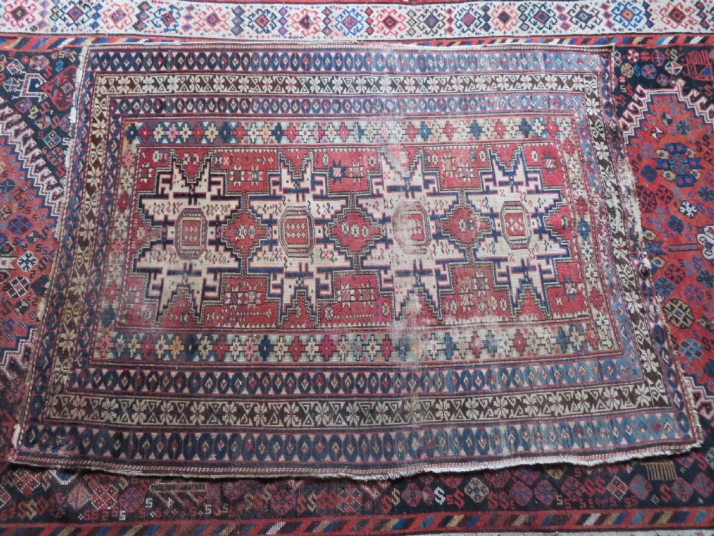 A distressed antique hand-knotted Caucasian Daghestan wool rug featuring geometric medallions and intricate borders in terracotta red, cream, and indigo blue. View XIII