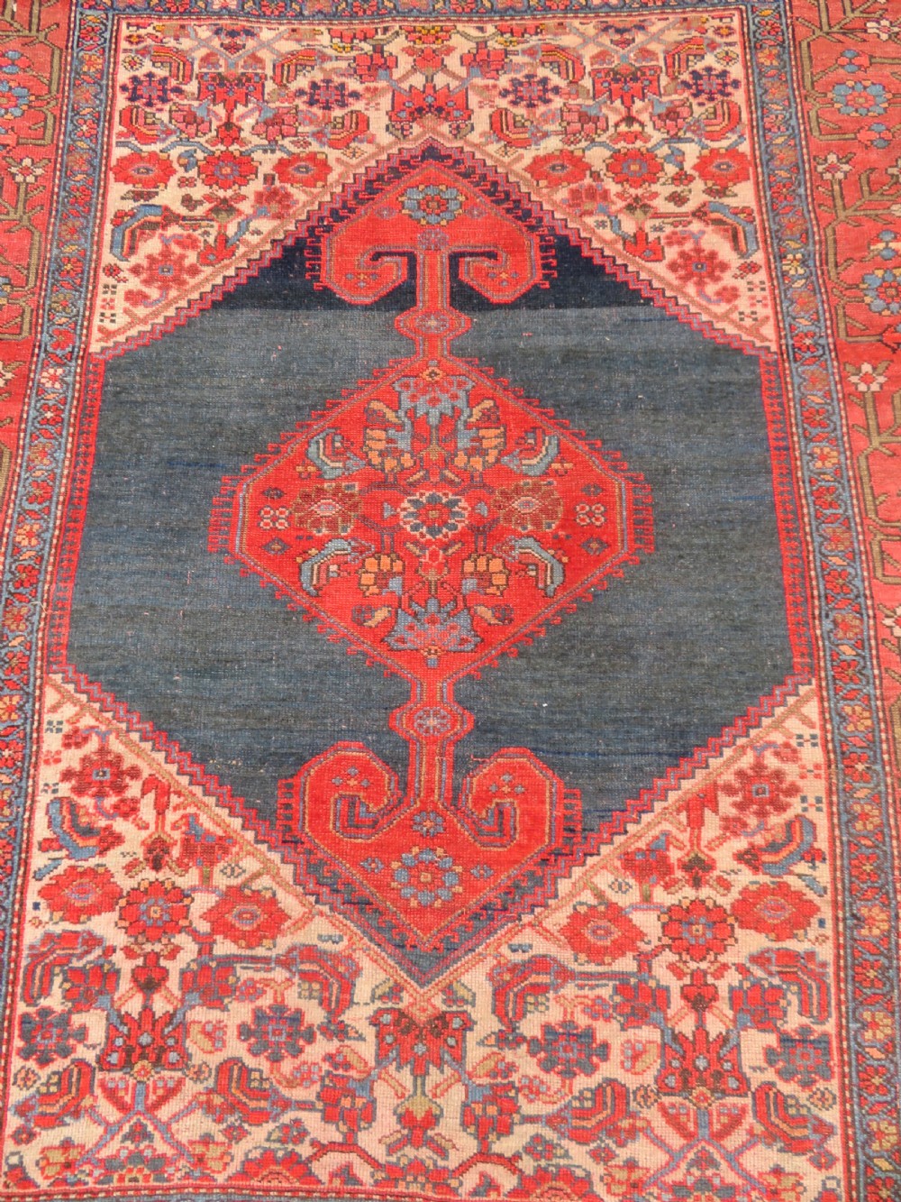 An antique hand-knotted Kurdish Bijar wool rug featuring a central red and blue medallion, cream patterned spandrels, and a terracotta floral border. View II
