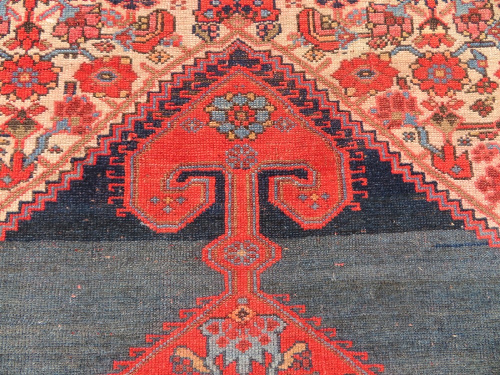 An antique hand-knotted Kurdish Bijar wool rug featuring a central red and blue medallion, cream patterned spandrels, and a terracotta floral border. View III