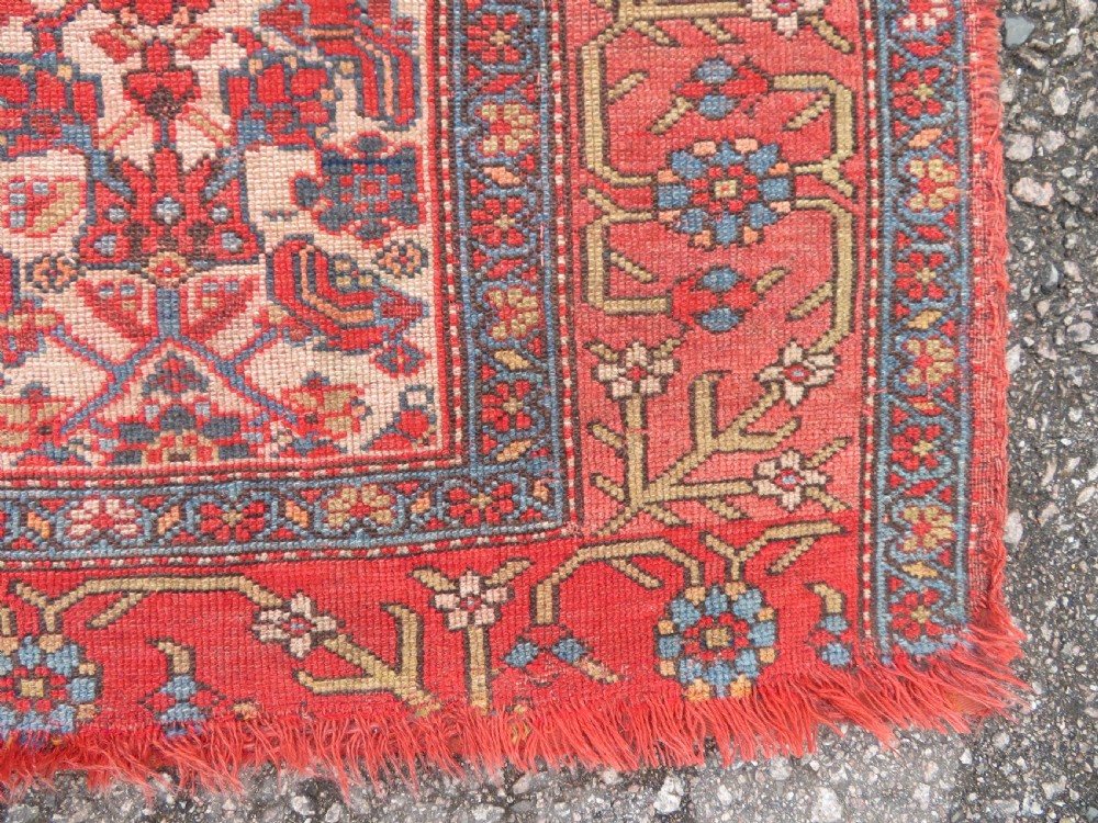 An antique hand-knotted Kurdish Bijar wool rug featuring a central red and blue medallion, cream patterned spandrels, and a terracotta floral border. View VI