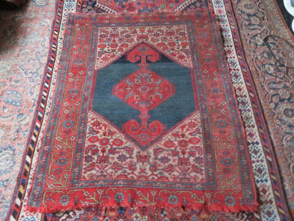 An antique hand-knotted Kurdish Bijar wool rug featuring a central red and blue medallion, cream patterned spandrels, and a terracotta floral border. View XV