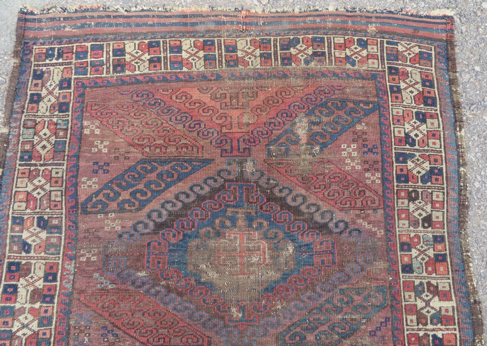 A rectangular distressed Persian Khamseh rug featuring repeating central diamond medallions in indigo blue and terracotta red surrounded by detailed geometric border bands. View II
