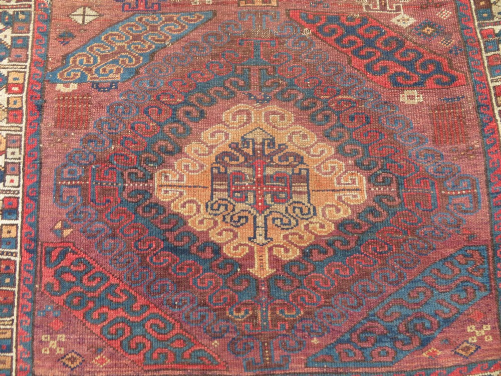 A rectangular distressed Persian Khamseh rug featuring repeating central diamond medallions in indigo blue and terracotta red surrounded by detailed geometric border bands. View III