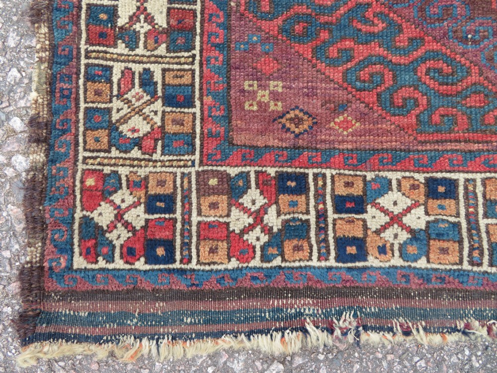 A rectangular distressed Persian Khamseh rug featuring repeating central diamond medallions in indigo blue and terracotta red surrounded by detailed geometric border bands. View VI