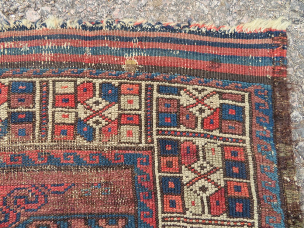 A rectangular distressed Persian Khamseh rug featuring repeating central diamond medallions in indigo blue and terracotta red surrounded by detailed geometric border bands. View VII
