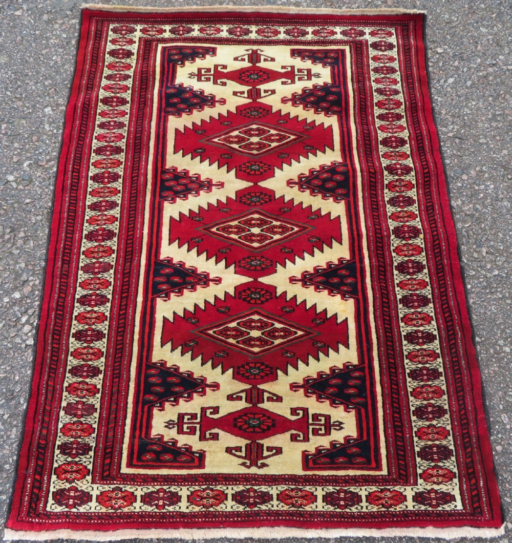 An antique rectangular hand-knotted Turkmen wool rug featuring red geometric diamond medallions on an ivory field with patterned dark borders.
