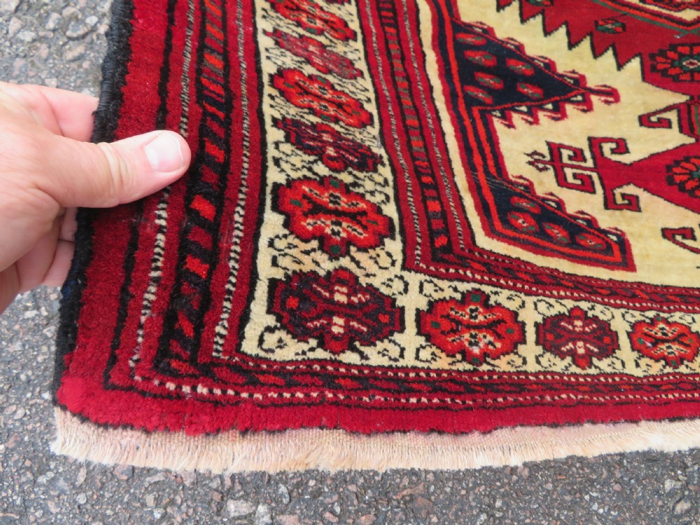An antique rectangular hand-knotted Turkmen wool rug featuring red geometric diamond medallions on an ivory field with patterned dark borders. View III