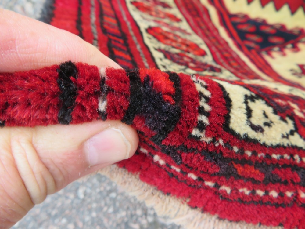 An antique rectangular hand-knotted Turkmen wool rug featuring red geometric diamond medallions on an ivory field with patterned dark borders. View IV