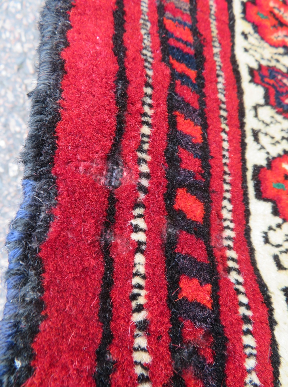 An antique rectangular hand-knotted Turkmen wool rug featuring red geometric diamond medallions on an ivory field with patterned dark borders. View V