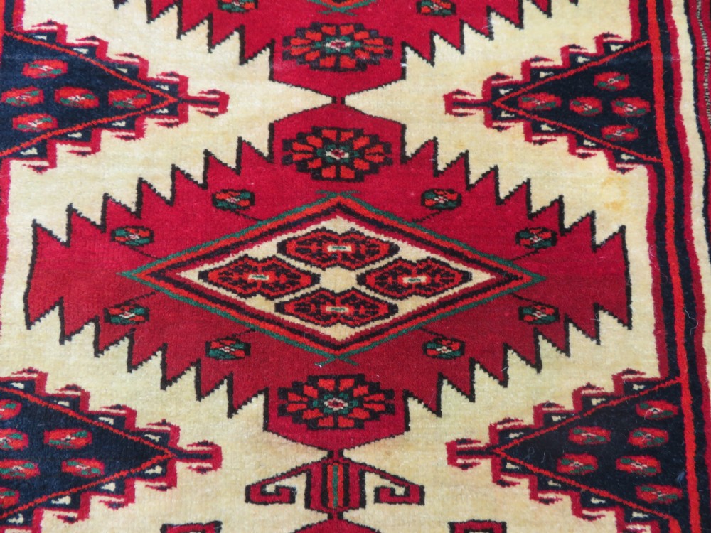 An antique rectangular hand-knotted Turkmen wool rug featuring red geometric diamond medallions on an ivory field with patterned dark borders. View VII