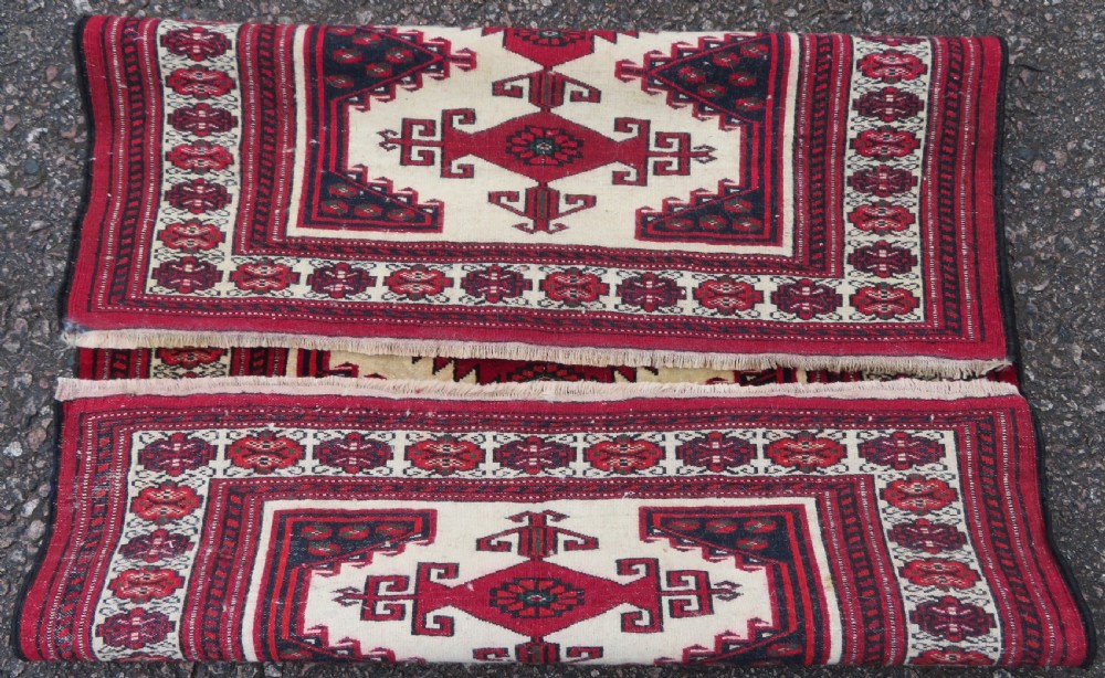 An antique rectangular hand-knotted Turkmen wool rug featuring red geometric diamond medallions on an ivory field with patterned dark borders. View X