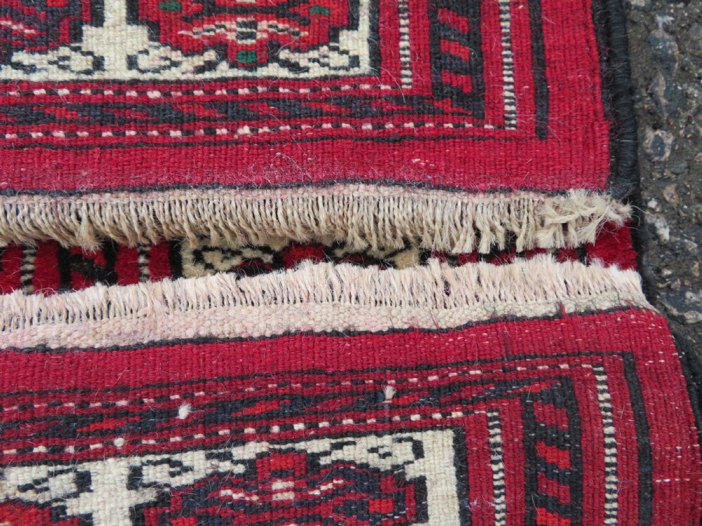 An antique rectangular hand-knotted Turkmen wool rug featuring red geometric diamond medallions on an ivory field with patterned dark borders. View XI