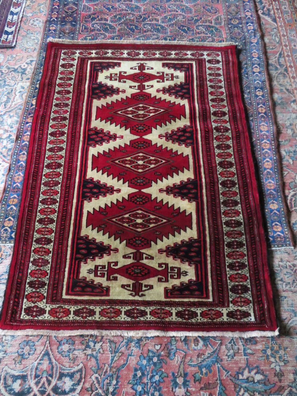 An antique rectangular hand-knotted Turkmen wool rug featuring red geometric diamond medallions on an ivory field with patterned dark borders. View XVI