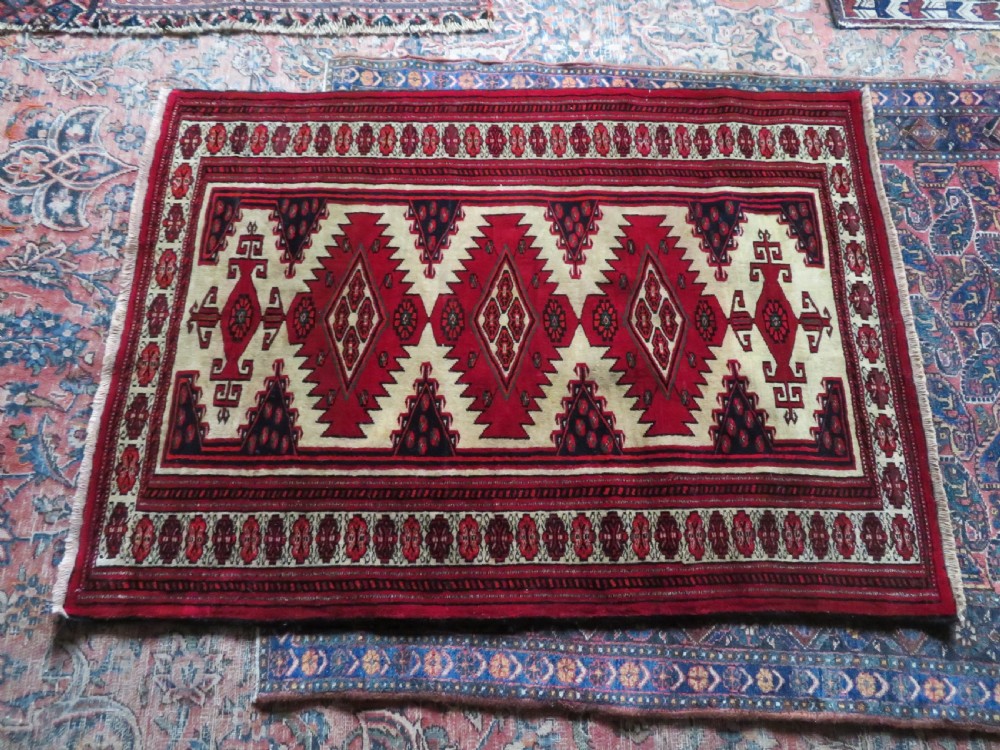 An antique rectangular hand-knotted Turkmen wool rug featuring red geometric diamond medallions on an ivory field with patterned dark borders. View XVII