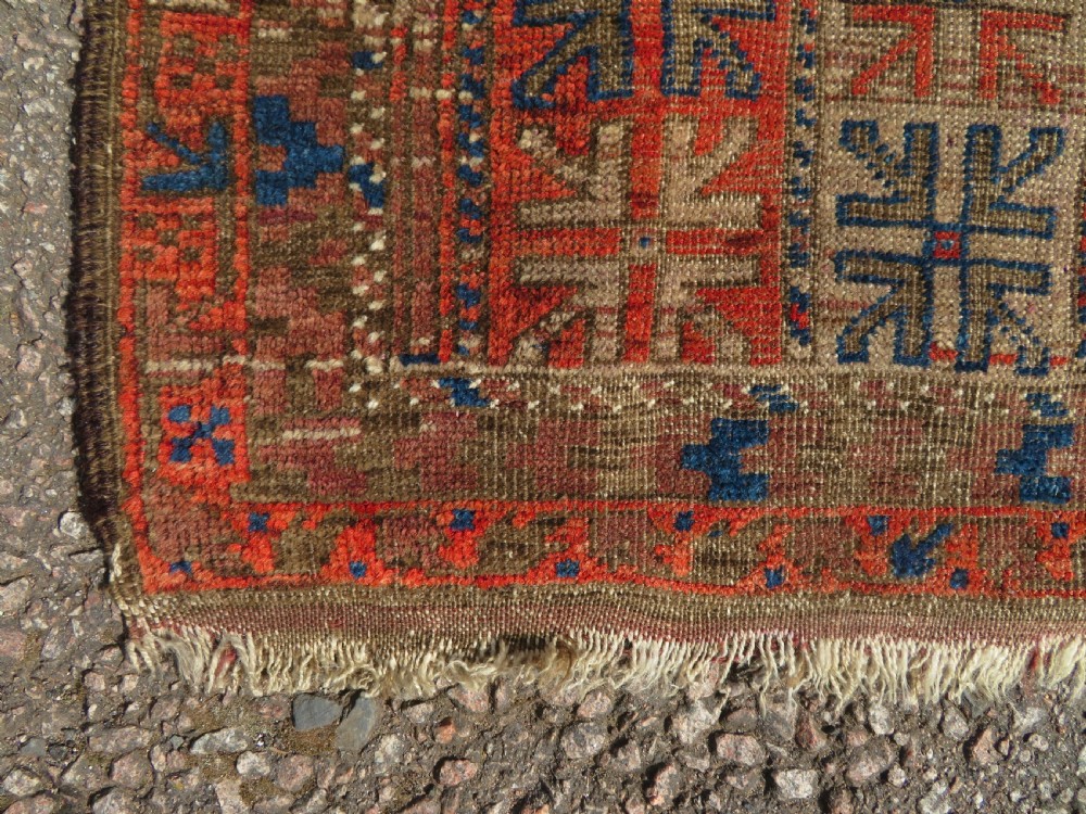 An antique hand-woven Baluch prayer rug showing distressed pile wear with geometric motifs in terracotta red, indigo, and deep brown. View II