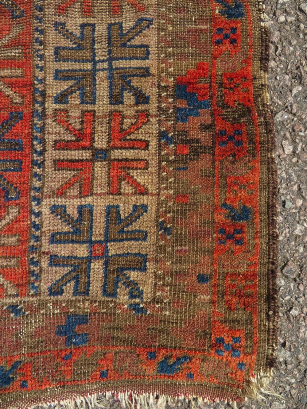 An antique hand-woven Baluch prayer rug showing distressed pile wear with geometric motifs in terracotta red, indigo, and deep brown. View IV