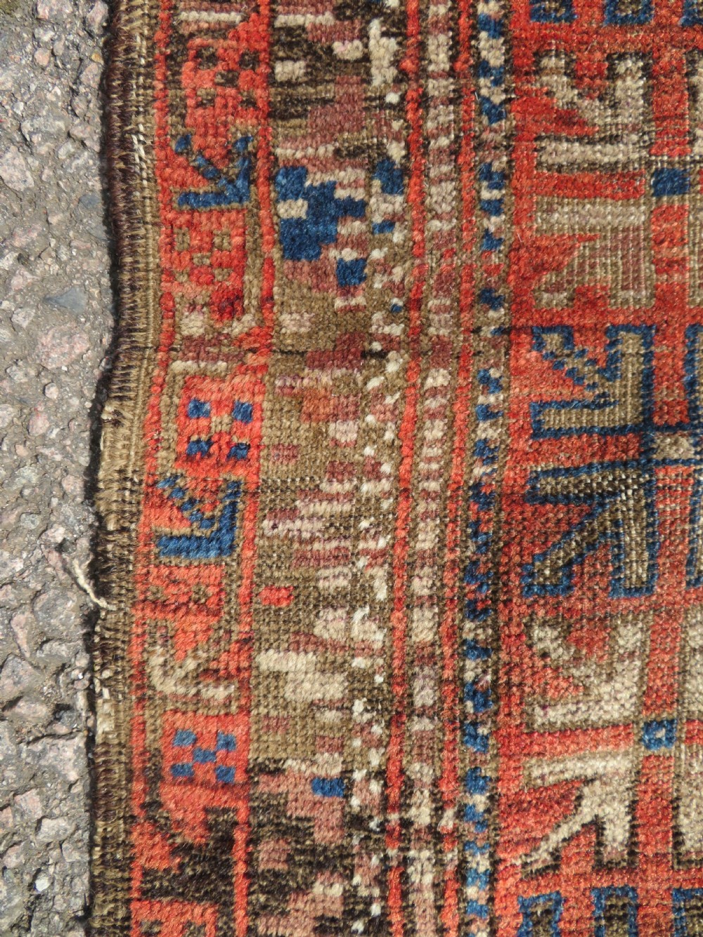 An antique hand-woven Baluch prayer rug showing distressed pile wear with geometric motifs in terracotta red, indigo, and deep brown. View V