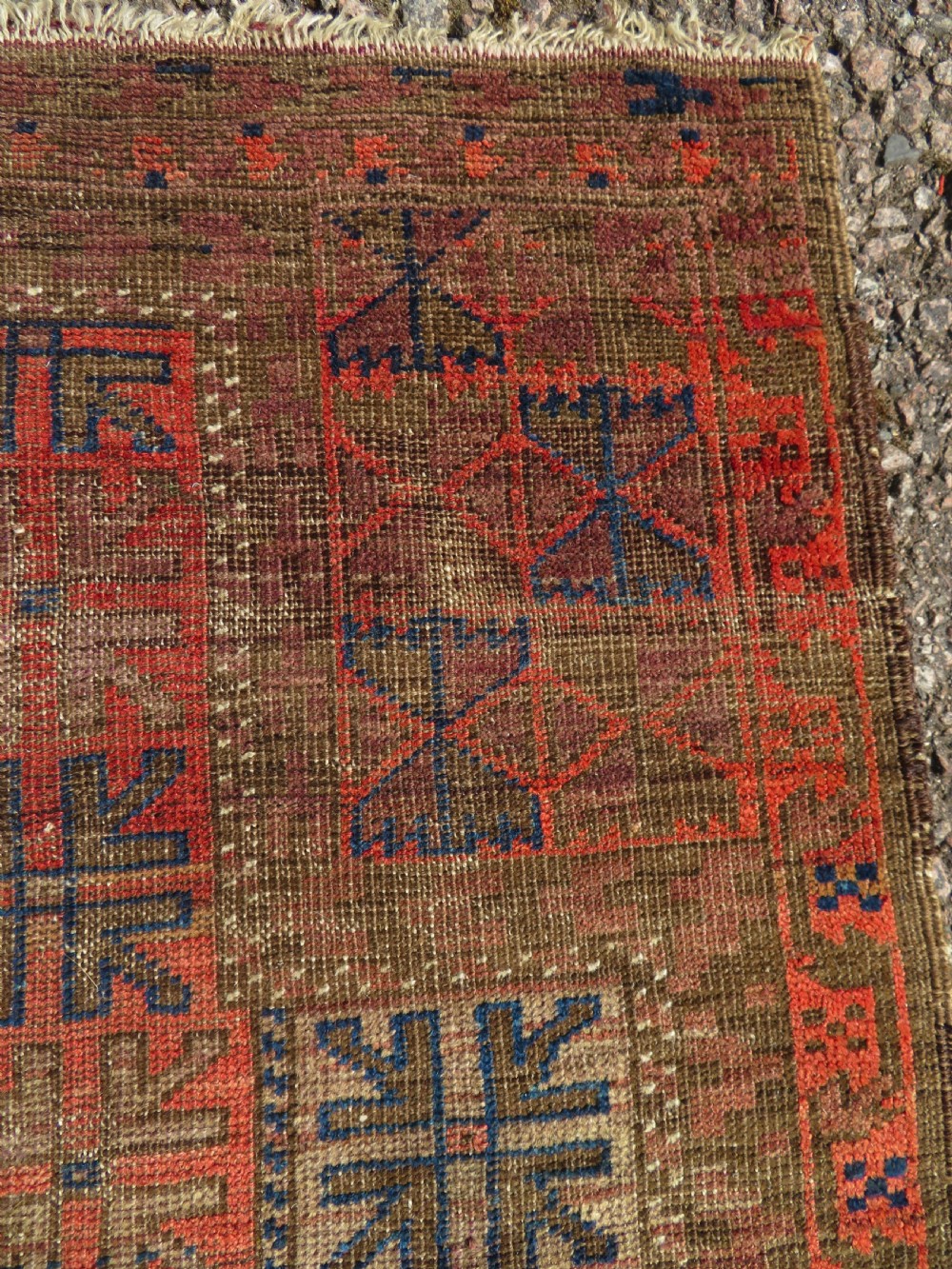 An antique hand-woven Baluch prayer rug showing distressed pile wear with geometric motifs in terracotta red, indigo, and deep brown. View VI