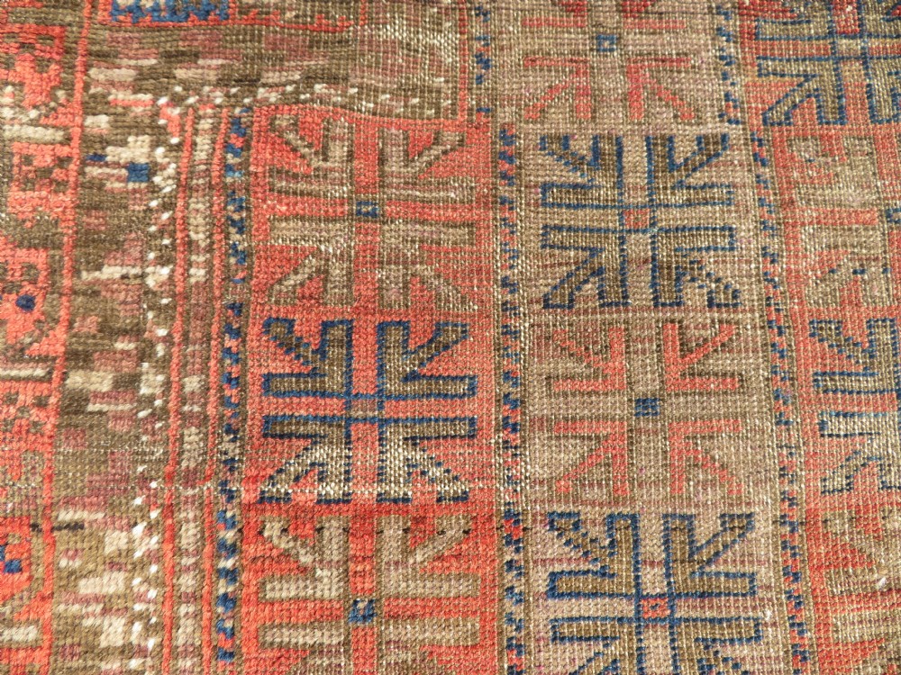An antique hand-woven Baluch prayer rug showing distressed pile wear with geometric motifs in terracotta red, indigo, and deep brown. View VII