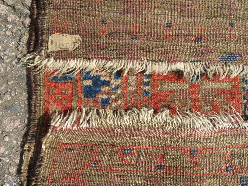 An antique hand-woven Baluch prayer rug showing distressed pile wear with geometric motifs in terracotta red, indigo, and deep brown. View IX
