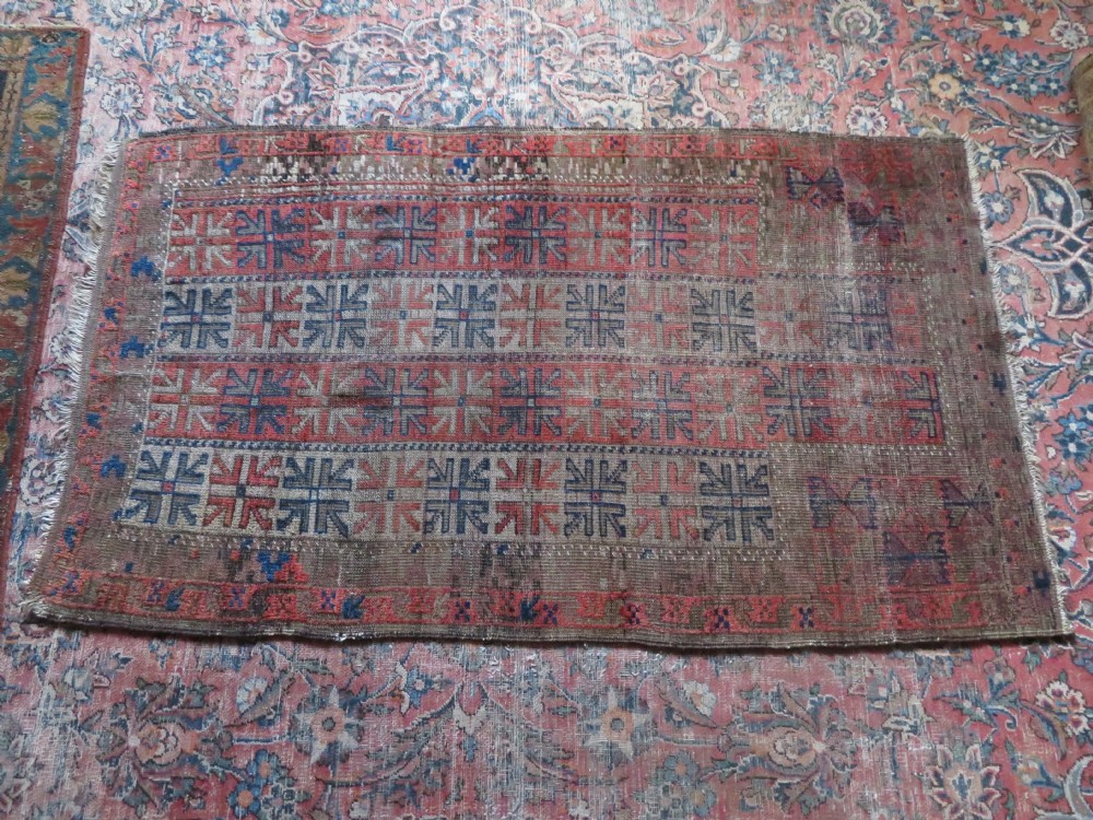 An antique hand-woven Baluch prayer rug showing distressed pile wear with geometric motifs in terracotta red, indigo, and deep brown. View XI