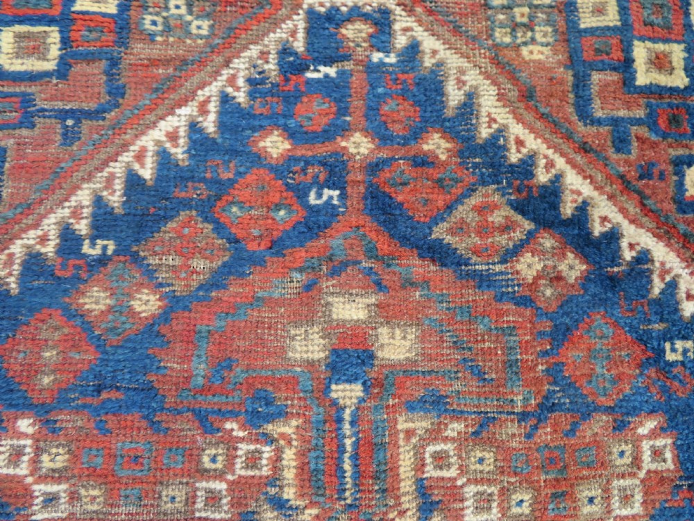 A small rectangular hand-knotted antique Khamseh rug featuring geometric tribal medallions in terracotta red, navy blue, and cream wool. View II