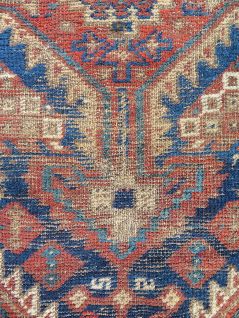A small rectangular hand-knotted antique Khamseh rug featuring geometric tribal medallions in terracotta red, navy blue, and cream wool. View III